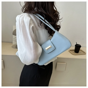 Close-up of a light blue leather baguette bag with golden buckle on a model's shoulder