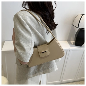 Detail of a chic beige baguette bag with a gold buckle worn as a shoulder bag