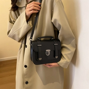 Retro black leather satchel bag with silver metal lock on a model in a beige trench coat