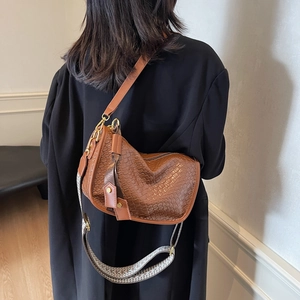 Sac demi-lune marron tressé avec bandoulière à motifs porté sur un manteau noir