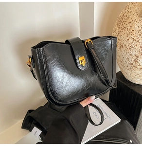 Detailansicht der schwarzen Eimertasche mit goldenen Beschlägen und glänzendem Leder