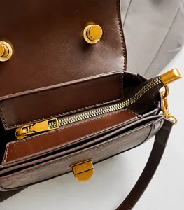 Detail of smooth golden zipper and magnetic closure on dark brown leather saddle bag