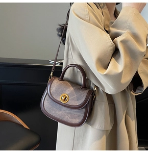 Close-up of retro brown crossbody bag with gold buckle and textured monogram pattern