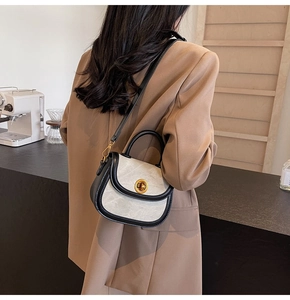 Detail of grey crossbody bag with gold buckle shown on model in a cafe setting