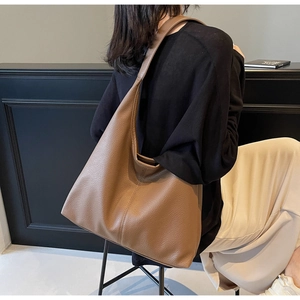 Brown litchi leather shoulder bag with wide strap on model in a minimalist room