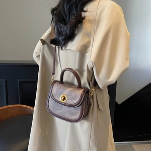Retro brown saddle bag with textured lid and gold lock on khaki trench coat model