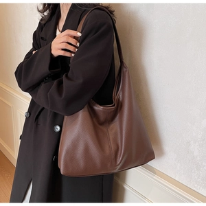 Close-up of a large dark brown pebbled leather tote bag worn over a black winter coat