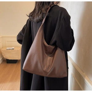 Large brown lychee grain leather tote bag shown on shoulder over a black wool coat