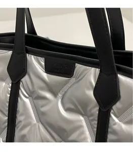 Close-up of silver quilted tote bag with black handles and a rectangular fashion label