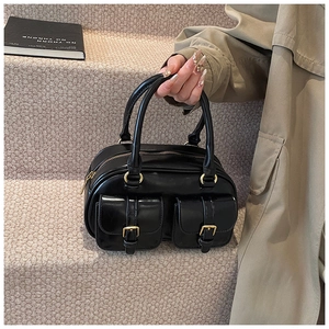 Detail of black mini Boston bag featuring high-gloss faux leather and dual front gold-buckle pockets