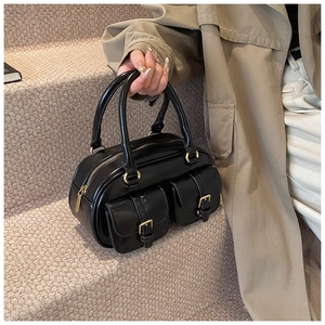Detail of a black bowling handbag with gold metal rings and dual front flap pockets