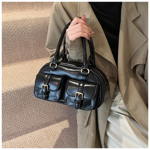 Detail of black glossy handbag with front utility pockets and gold metal hardware