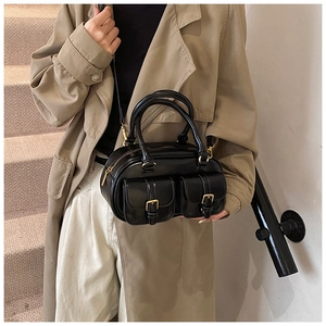 Detail of black glossy handbag with gold metal buckles on front pockets and top handles