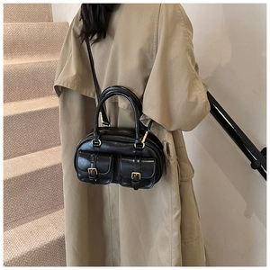 Detailed view of a black leather handbag with gold hardware on a beige trench coat