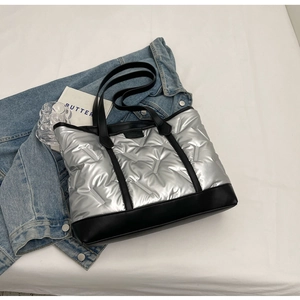Detail of silver quilted tote bag with black leather straps and down padding texture