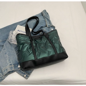 Detail of dark green quilted tote bag with black leather straps on a minimalist background