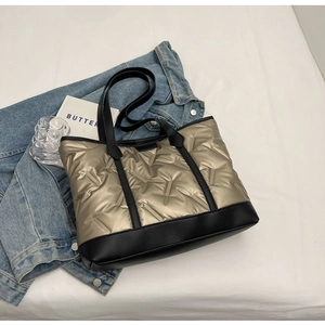 Detail of gold quilted tote bag with black leather base on blue denim background