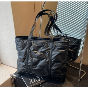 Detail of black quilted puffer tote bag with a leather fashion tag on a display table