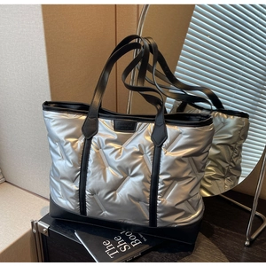 Close-up of silver quilted tote bag with metallic finish and black faux leather logo patch