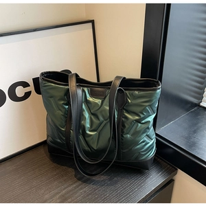 Detail of dark green quilted tote bag with black leather trim on a modern grey surface