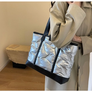 Quilted silver tote bag with padded texture and black leather details on a stylish model