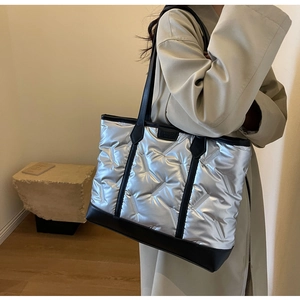 Detail shot of large silver quilted tote bag with black handles on a fashion model