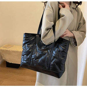Quilted black tote bag with metallic diamond texture shown on shoulder in a warm interior