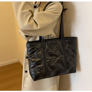 Detailed view of black quilted tote bag with fashion label on elegant beige trench coat