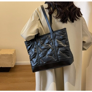 Detailed side view of a black quilted tote bag worn by a model in a beige trench coat