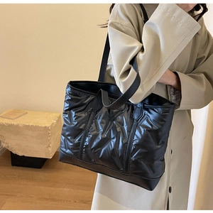 Detailed view of black quilted tote bag with glossy texture worn by a model