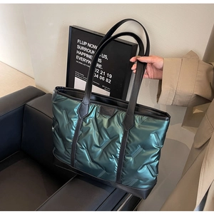 Detail of dark green quilted tote bag featuring black leather handles and glossy texture