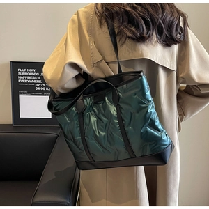 Detail of dark green quilted tote bag with metallic sheen and black leather accents