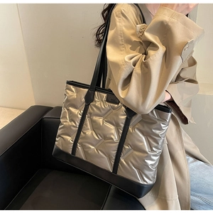 Detail view of quilted champagne gold tote bag with black leather straps and brand label