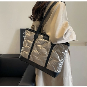 Model wearing a large champagne gold quilted puffer tote bag with black leather straps