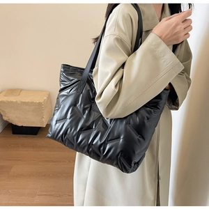 Grand sac cabas matelassé noir à texture rembourrée porté à l'épaule par un mannequin chic