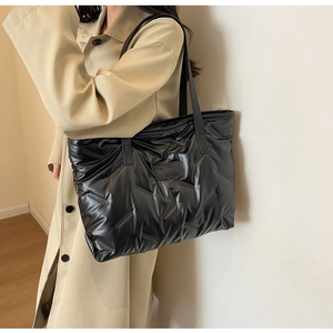 Détail du sac fourre-tout matelassé noir brillant avec écusson logo sur le devant