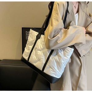 Detail of quilted puffer tote bag with black strap and contrast base on white surface