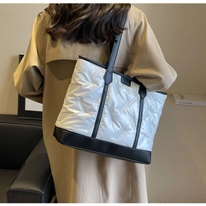 Detail of white quilted puffer tote bag with black leather straps and brand logo plate