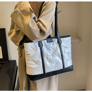 Detail of quilted white tote bag with black leather straps and fashion label tag