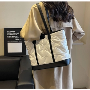Close-up of white quilted tote bag featuring black leather trim and shoulder straps