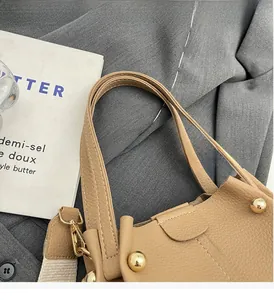 Close-up of camel lychee texture bucket bag with gold spherical metal hardware and woven strap