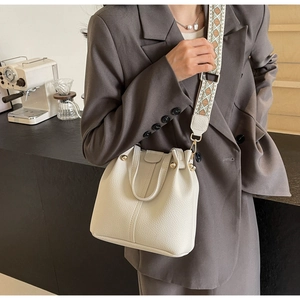 Detail of cream bucket bag with textured leather and patterned wide shoulder strap