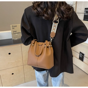Brown leather bucket bag detail with vintage embroidered wide strap on a person