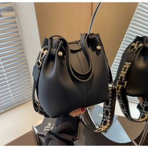 Detail of black lychee leather bucket bag with gold accents and geometric wide strap