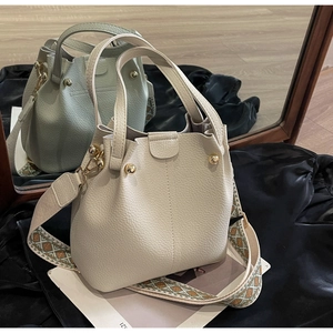 Detail of cream pebbled leather bucket bag with colorful woven strap and gold studs