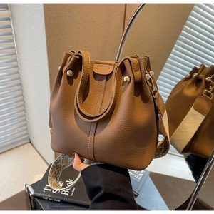 Detail of brown litchi leather bucket bag featuring a woven geometric wide shoulder strap
