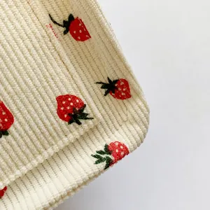 Macro view of cream corduroy fabric featuring detailed red strawberry embroidery work