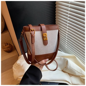 Detail of canvas bucket bag showing retro leather trim and golden metal turn-lock closure
