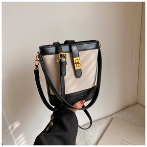 Detail of canvas bucket bag with black leather trim and gold rotary clasp closure