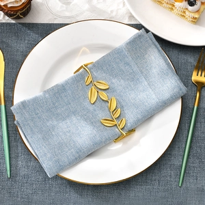 Golden leaf napkin ring with intricate vein details on a light blue linen napkin